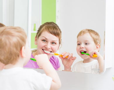 Happy mother and child teeth brushing in bathroom front of mirr